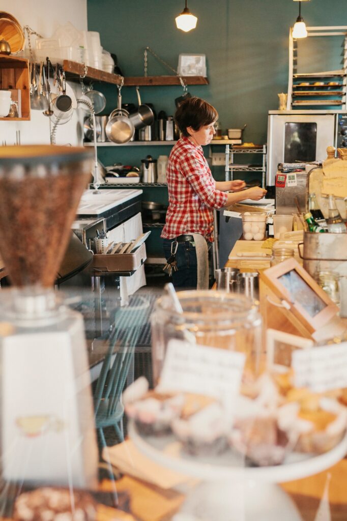 Femme barista en chemise à carreaux travaillant derrière le comptoir d’un café local en Ardèche – image illustrant l’artisanat, le commerce de proximité et l’ambiance chaleureuse des entreprises locales